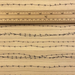 May include: A beige fabric with a repeating pattern of black barbed wire. A wooden ruler with inch markings is placed on top of the fabric.