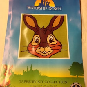 May include: A tapestry kit featuring a close-up of a brown rabbit's face with orange ears and a green background. The kit is part of the "Watership Down" collection and is 15 inches by 15 inches.