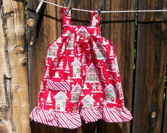 Puede incluir: Vestido rojo con estampado de casas de jengibre, colgado de un tendedero. El vestido tiene un dobladillo con volantes y rayas rojas y blancas de bastón de caramelo. Las correas también son rojas.