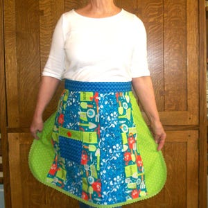 May include: A blue and green gardening apron with a variety of gardening tools and the word "SEEDS" printed on it. The apron has a blue waistband and a green scalloped edge. The apron is made of cotton.