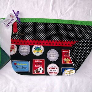 Peut inclure: Tablier de professeur noir avec une bordure et des bretelles vertes. Le tablier pr&eacute;sente un motif &agrave; pois noirs et blancs, un ruban &agrave; pois rouges et des &eacute;cussons avec les mentions "Meilleur professeur du monde" et "Mon professeur pr&eacute;f&eacute;r&eacute;".