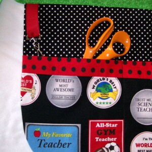 Peut inclure: Tablier noir &agrave; pois blancs, bordure rouge et accents verts. Poches avec &eacute;cussons indiquant &laquo;&nbsp;Meilleur professeur du monde&nbsp;&raquo;, &laquo;&nbsp;Mon professeur pr&eacute;f&eacute;r&eacute;&nbsp;&raquo; et &laquo;&nbsp;Professeur de gym All-Star&nbsp;&raquo;. Ciseaux orange dans une poche.