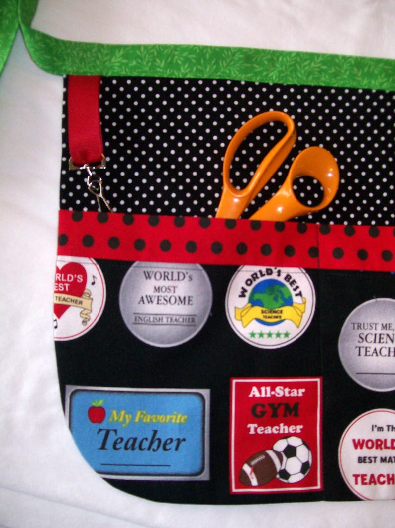 Peut inclure: Tablier noir &agrave; pois blancs, bordure rouge et accents verts. Poches avec &eacute;cussons indiquant &laquo;&nbsp;Meilleur professeur du monde&nbsp;&raquo;, &laquo;&nbsp;Mon professeur pr&eacute;f&eacute;r&eacute;&nbsp;&raquo; et &laquo;&nbsp;Professeur de gym All-Star&nbsp;&raquo;. Ciseaux orange dans une poche.