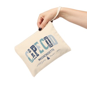 May include: A beige canvas zippered pouch with a blue and white graphic design that says "CAPE COD MASSACHUSETTS" with a lighthouse and sailboat image.