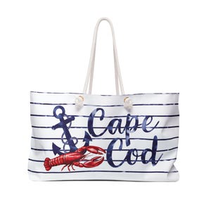 Puede incluir: Bolsa de lona blanca con rayas azules y blancas. La bolsa tiene un ancla azul marino y una langosta roja con el texto "Cape Cod" en azul marino.