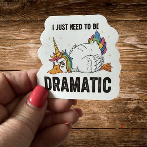 May include: A white sticker featuring a cartoon duck with a rainbow-colored unicorn horn, mane, and tail. The duck has an annoyed expression and is lying down. The text reads I JUST NEED TO BE DRAMATIC in bold black capital letters.