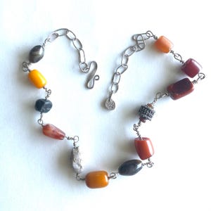 May include: A necklace featuring a variety of colorful beads in shades of yellow, orange, red, gray, and black. The beads are strung together with a silver chain and wire, creating a unique and eye-catching accessory.
