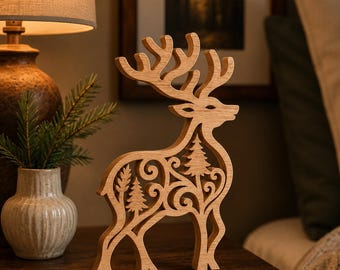 May include: A light brown wooden cutout of a standing deer featuring intricate scrollwork and small pine tree silhouettes within its body. The deer has large, branching antlers and is positioned upright, showcasing a smooth, natural wood grain finish.