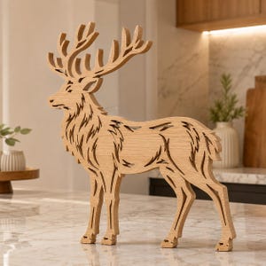 May include: A light brown wooden cutout of a standing deer with large, detailed antlers. The figure features intricate, laser-cut patterns throughout its body, showcasing the natural wood grain texture and a clean, flat profile design.
