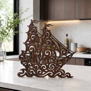 Puede incluir: Una escultura de madera tallada en color marrón oscuro que representa un velero con intrincados adornos y patrones de remolinos que simulan olas y velas. La pieza decorativa cuenta con una base plana y recortes detallados en toda su estructura.