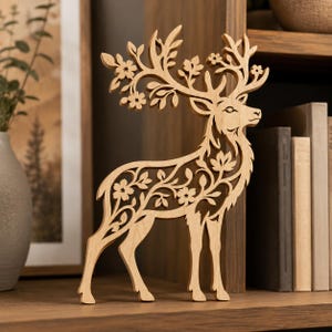 May include: A light-colored wooden cutout of a standing deer with intricate laser-cut details. The deer features elaborate floral and leaf patterns integrated into its body and large antlers, creating a delicate, openwork silhouette design.