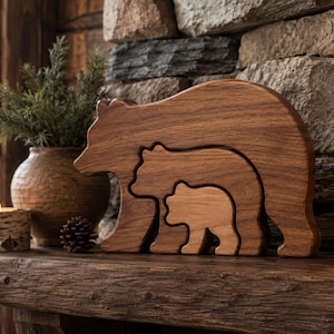 May include: A set of three nested wooden bear figurines carved from smooth, medium-brown wood. The design features a large adult bear silhouette containing a medium-sized bear and a smaller bear cub, all standing in a profile orientation.