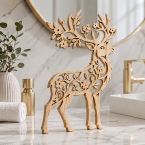 May include: A light brown wooden deer figurine featuring intricate laser-cut floral and leaf patterns throughout its body and antlers. The deer stands in a profile position, showcasing a detailed cutout design that forms the shape of the animal.