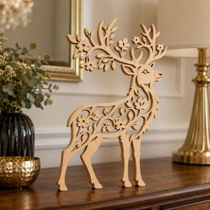 May include: A light brown wooden deer figurine featuring intricate laser-cut details of flowers and leaves integrated into its body and antlers. The cutout design creates a delicate silhouette of a standing deer with a smooth, natural wood finish.