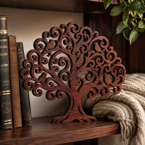 Peut inclure: Une sculpture en bois découpé brun foncé représentant un arbre avec des branches en volutes complexes et quatre petits oiseaux perchés dans la canopée. L'arbre présente un tronc solide et un sommet arrondi, avec un design découpé au laser.