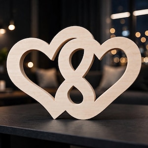 May include: A light-colored wooden cutout featuring two interlocking heart shapes that form an infinity symbol in the center. The smooth, flat surface of the wood displays a natural grain pattern, and the object is shaped as a single continuous piece.
