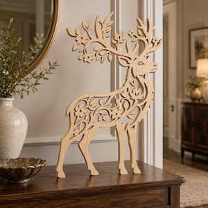 May include: A light-colored wooden cutout of a standing deer featuring intricate laser-cut details of flowers and leaves integrated into its body and antlers. The deer is depicted in profile, showcasing a smooth, flat surface and natural wood grain.