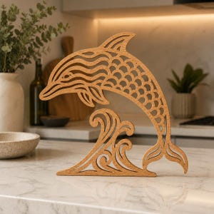 Peut inclure: Une découpe en bois brun clair représentant un dauphin sautant au-dessus d'une vague. Le dauphin présente des motifs complexes découpés au laser, incluant des lignes ondulées sur la tête et un motif en écailles sur le corps, formant une silhouette.