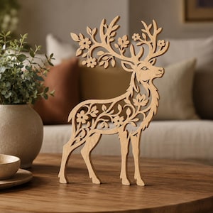 May include: A light brown wooden cutout of a standing deer featuring intricate laser-cut details of leaves and flowers integrated into its body and antlers. The deer is depicted in profile, showcasing a delicate, openwork design throughout its form.