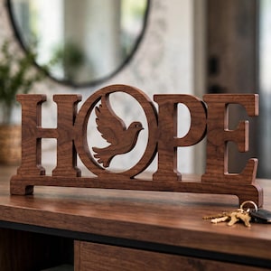 May include: A dark brown wooden sign featuring the word HOPE in capital letters, with a cutout of a flying dove replacing the letter O. The sign is mounted on a rectangular base and stands upright, displaying a natural wood grain texture throughout.