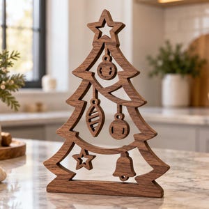 May include: A dark brown wooden cutout in the shape of a Christmas tree. The tree features a star at the top and various hanging ornaments including spheres, a bell, and a smaller star, all carved from a single piece of wood with a flat base.