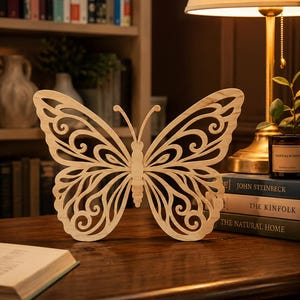 May include: A light-coloured wooden butterfly cutout featuring intricate, symmetrical scrollwork patterns throughout its wings. The butterfly has two slender antennae and a segmented body, standing upright with a natural wood grain finish.