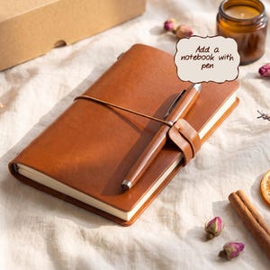 May include: A tan leather notebook with a matching pen secured by a leather strap. A speech bubble graphic above the notebook contains the text Add a notebook with pen. The notebook has a smooth finish and is positioned at an angle.