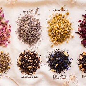 May include: Eight distinct piles of loose-leaf tea and dried botanicals arranged in two rows. The top row features Dried Rose, Lavander, Chamomile, and Hibiscus. The bottom row includes 40 Winks, Masala Chai, Earl Grey Bella Luna, and Butterscotch tea.