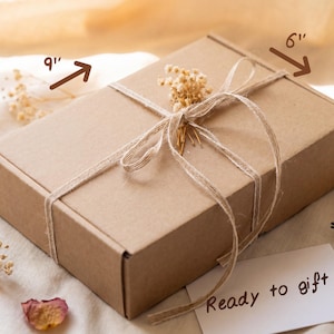 May include: A rectangular brown cardboard box tied with thin twine and decorated with a small sprig of dried white flowers. The box dimensions are labeled as 9 inches long, 6 inches wide, and 3 inches high. A white card with the text Ready to gift.