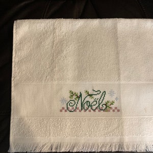 May include: White hand towel with a green and red embroidered design that says "Noel" with snowflakes and holly.