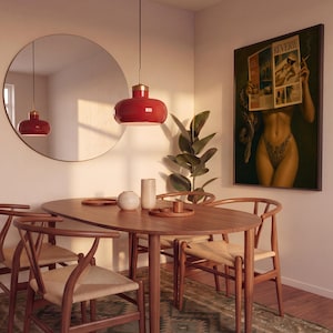 Op de afbeelding: Een eetkamerset bestaande uit een ovale houten tafel met vier stoelen met gevlochten zittingen, een grote ronde spiegel, een rode hanglamp en een ingelijste wandprint getiteld Reverie met een persoon die een tijdschrift en een slang vasthoudt.