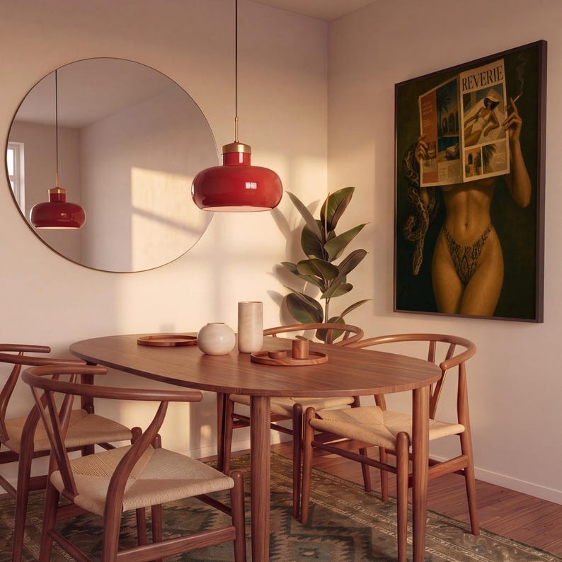 Op de afbeelding: Een eetkamerset bestaande uit een ovale houten tafel met vier stoelen met gevlochten zittingen, een grote ronde spiegel, een rode hanglamp en een ingelijste wandprint getiteld Reverie met een persoon die een tijdschrift en een slang vasthoudt.