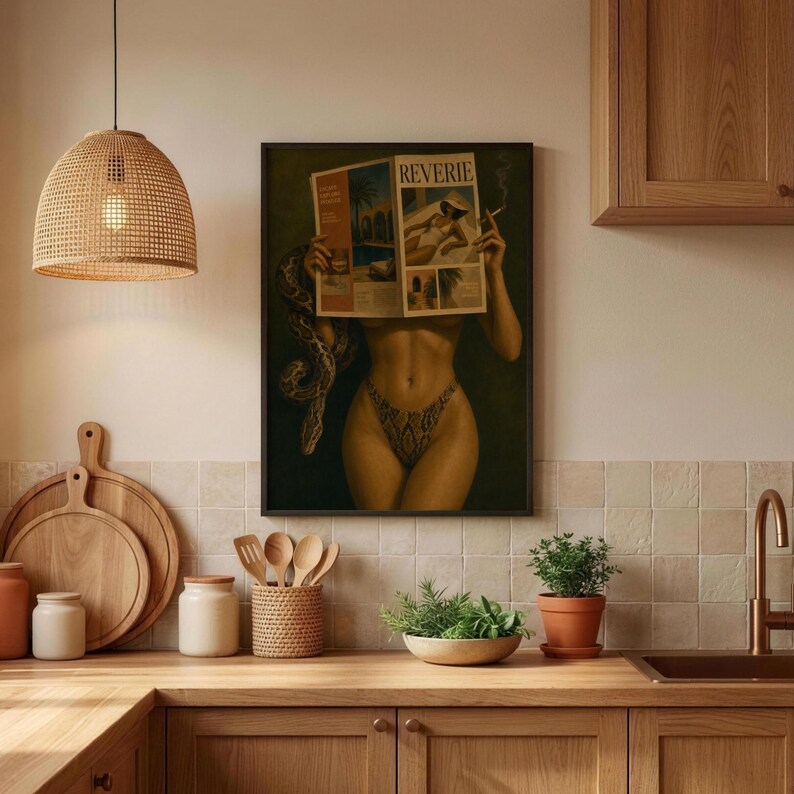 Op de afbeelding: Een ingelijste kunstdruk van een persoon die een tijdschrift genaamd REVERIE vasthoudt, met een slang om de arm gewikkeld. De persoon draagt een bikinibroekje met patroon. Het kunstwerk hangt in een keuken met houten kasten en een rieten lamp.