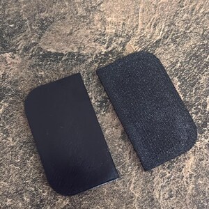 May include: Two rectangular black components with rounded corners on one side. One piece features a smooth, matte finish, while the other piece displays a textured, cross-hatched surface pattern. Both items are flat and uniform in shape.