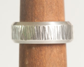 May include: A silver ring with a textured, hammered finish. The ring is wide and has a rounded profile.