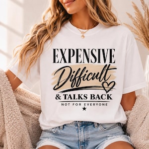 May include: A white short-sleeved t-shirt featuring black text that reads EXPENSIVE, Difficult, & TALKS BACK, NOT FOR EVERYONE. The design includes a beige brushstroke background behind the word Difficult and a small black heart and star.