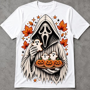 May include: A white t-shirt featuring a graphic of a hooded figure with a mask holding a ghost-shaped cookie and a tray of three jack-o'-lantern cookies. The design includes orange maple leaves and small stars surrounding the central figure.