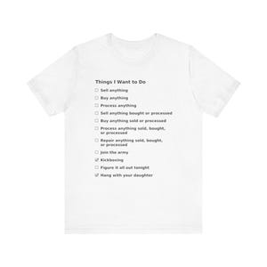 May include: A white short-sleeve t-shirt featuring a black printed checklist titled Things I Want to Do. The list includes items like Sell anything, Buy anything, Process anything, Join the army, and checked boxes for Kickboxing and Hang with your daughter.