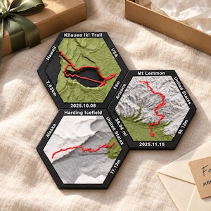 May include: Three hexagonal 3D topographic map tiles featuring Kilauea Iki Trail, Mt Lemmon, and Harding Icefield. Each black-framed tile displays a red trail path, location names, dates, and distances in miles or meters, showcasing terrain details.