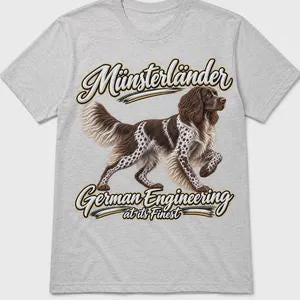 May include: A light gray t-shirt featuring a graphic of a brown and white spotted Münsterländer dog. Above the dog, the text reads Münsterländer, and below the dog, the text reads German Engineering at its Finest in a stylized script font.