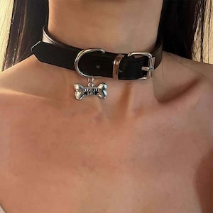 Peut inclure: Un collier ras-du-cou en cuir noir doté d'une boucle en métal argenté et d'une breloque pendante en forme d'os de chien avec un motif de patte découpé au centre. Le collier est fixé par une boucle ardillon en métal et un passant.