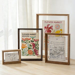 Peut inclure: Quatre cadres flottants en bois de tailles variées contenant des impressions artistiques. Un cadre contient un dessin au trait d'un oiseau, un autre une impression florale étiquetée Flower Market Bologna, un troisième Flower Market et une partition.