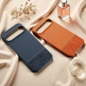 Puede incluir: Dos fundas rectangulares para teléfono, una azul oscuro y otra naranja, con una sección superior texturizada y un panel inferior liso. Cada funda tiene un recorte grande en la parte superior para el módulo de la cámara.