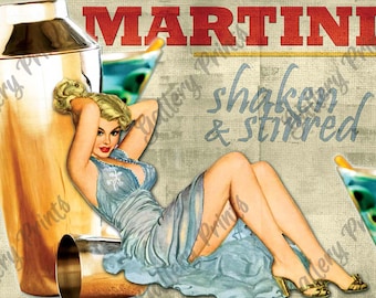 May include: A decorative print featuring a blonde person in a light blue dress reclining next to a large gold cocktail shaker and a martini glass. The text MARTINI appears in red at the top, with the words shaken & stirred in blue script below.