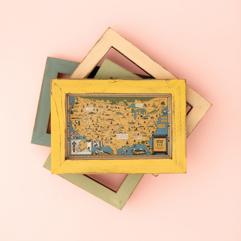 Puede incluir: Un marco de madera amarillo con un mapa vintage de los Estados Unidos en su interior. El mapa est&aacute; rodeado por un borde azul claro y presenta varias ilustraciones de monumentos y ciudades. El marco est&aacute; superpuesto a otros dos marcos, uno verde claro y otro marr&oacute;n claro.