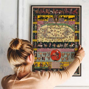 Puede incluir: Un p&oacute;ster vintage enmarcado con una colorida ilustraci&oacute;n de una escena de rodeo. La obra de arte presenta vaqueros a caballo, eventos de rodeo y varias ilustraciones de equipos de rodeo. El p&oacute;ster tiene un marco negro y lo sostiene una persona.