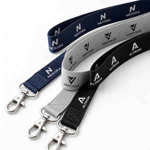 Op de afbeelding: Drie stoffen keycords in marineblauw, lichtgrijs en zwart. Elk keycord is voorzien van een herhalend wit logo en merknaam: Nexora voor de marineblauwe, Vantage voor de grijze en Altrion voor de zwarte. Elke band heeft een zilverkleurige metalen karabijnhaak.