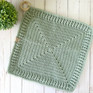 May include: A sage green crocheted square with a decorative border. The square is made with a simple stitch pattern and has a subtle texture.