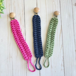 May include: Three crocheted baby teethers with wooden clips. The teethers are pink, navy blue, and green.