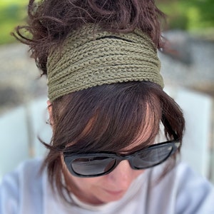 Puede incluir: Una mujer con un diadema de ganchillo verde y gafas de sol negras. Su cabello está recogido en un moño desordenado.